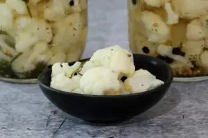 cauliflower pickles in a small bowl with jars in the background.