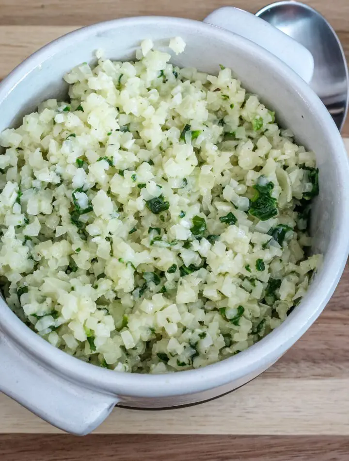 A bowl of cauliflower rice with garlic, parmesan cheese, and parsley