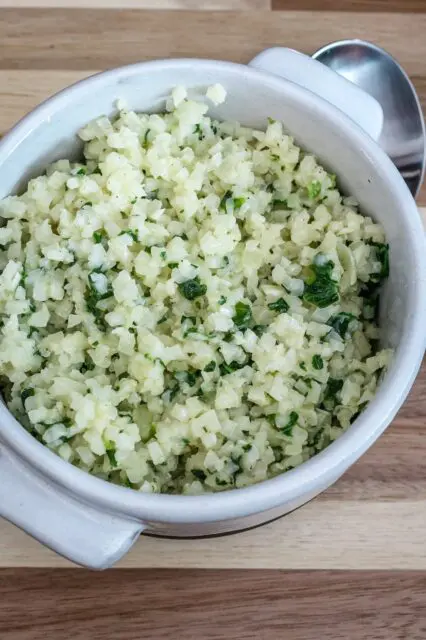 A bowl of cauliflower rice with garlic, parmesan cheese, and parsley