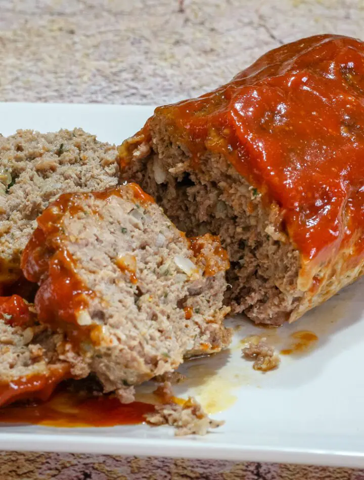 A tasty loaf of cheddar and tomato soup meatloaf on a platter, sliced.