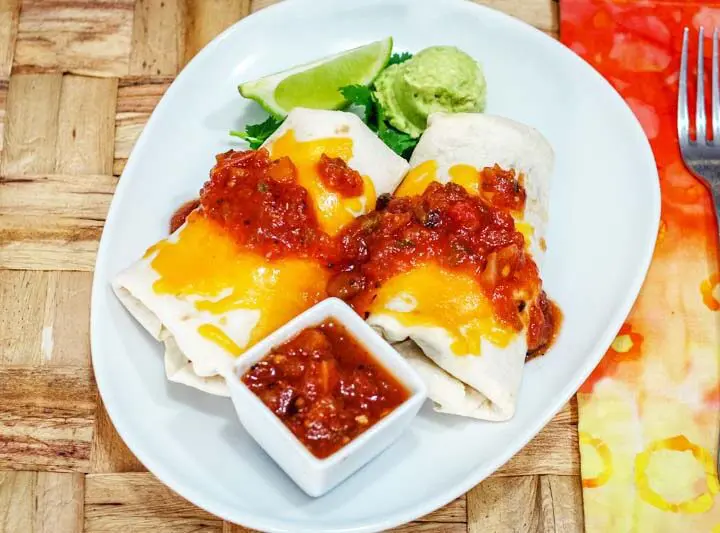 chicken burritos on a plate with salsa and guac