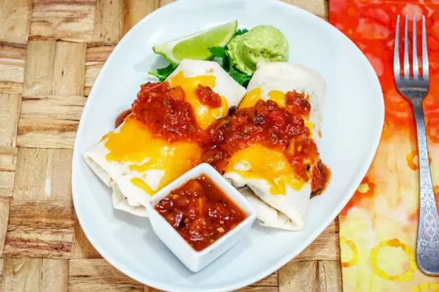 chicken burritos on a plate with salsa and guac