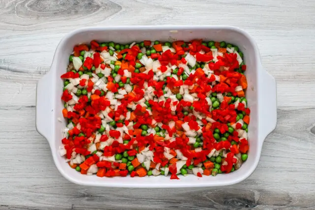 Chicken pot pie casserole prep: Layers of peas and carrots, onions, and pimientos.