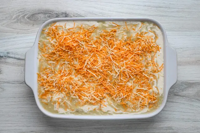 Chicken pot pie casserole prep: Layer of biscuit mixture, broth and condensed soup, and cheese, ready to bake.