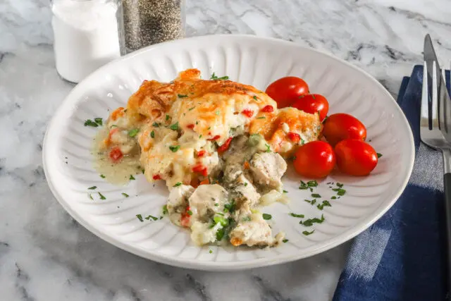 A plate with a helping of chicken pot pie casserole with a garnish of parsley and some grape tomatoes on the side.