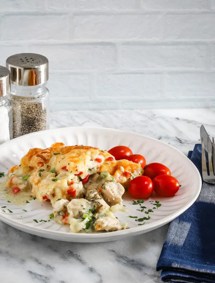 A plate with a helping of chicken pot pie casserole with a garnish of parsley and some grape tomatoes on the side.