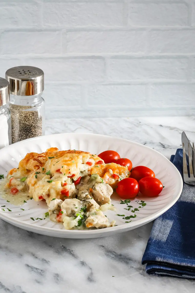 A plate with a helping of chicken pot pie casserole with a garnish of parsley and some grape tomatoes on the side.