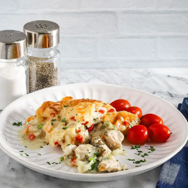 A plate with a helping of chicken pot pie casserole with a garnish of parsley and some grape tomatoes on the side.