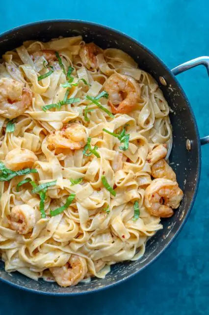 shrimp fettuccine in a skillet with chile crisp and basil garnish