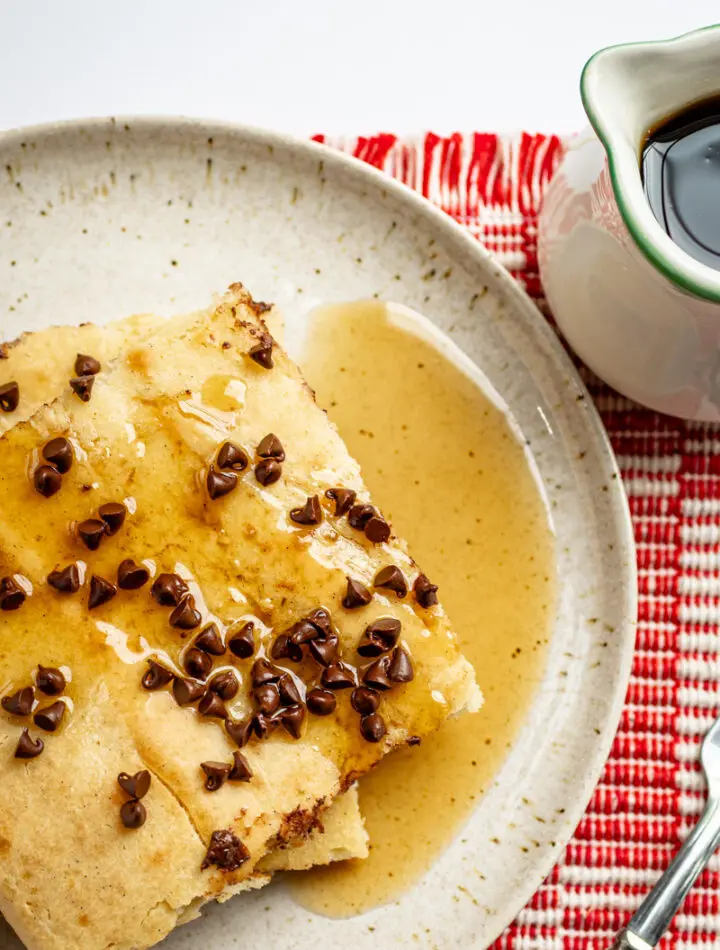 Slices of sheet pan pancakes on a plate with chocolate chip topping and syrup on the side.