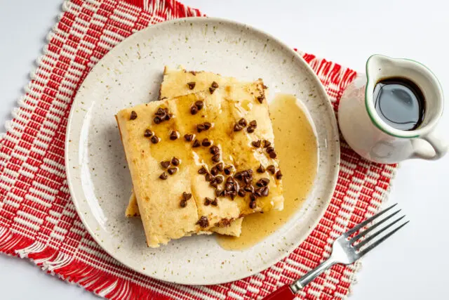 Slices of sheet pan pancakes on a plate with chocolate chip topping and syrup on the side.