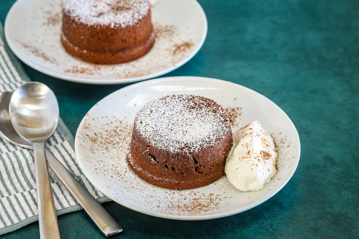 Chocolate fondants on plates with whipped cream and a dusting of cocoa and powdered sugar.