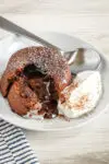 A chocolate fondant, also known as molten lava cake, on a plate with freshly whipped cream and a light dusting of cocoa and powdered sugar.