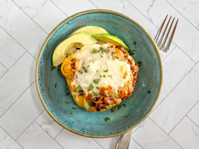 A serving of chorizo stuffed peppers with some sliced avocado.