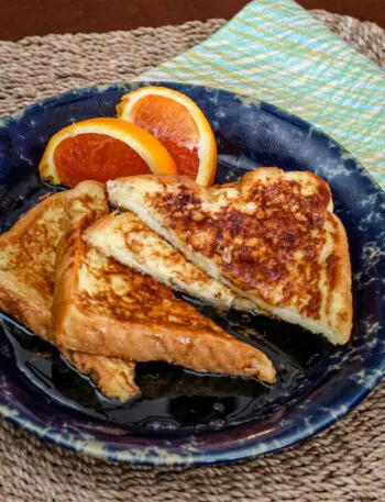 sliced French toast on a plate with orange wedges on the side.