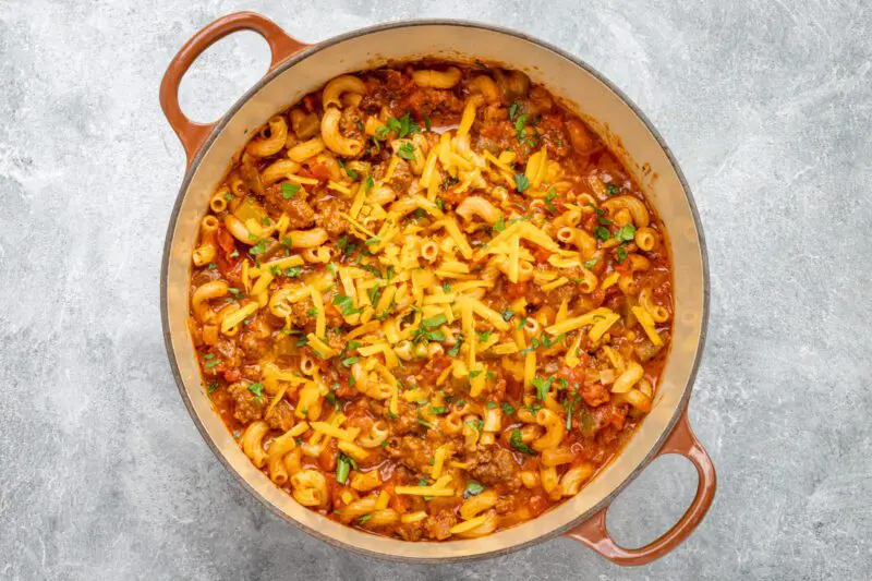 goulash in a dutch oven with a garnish of cheese and basil