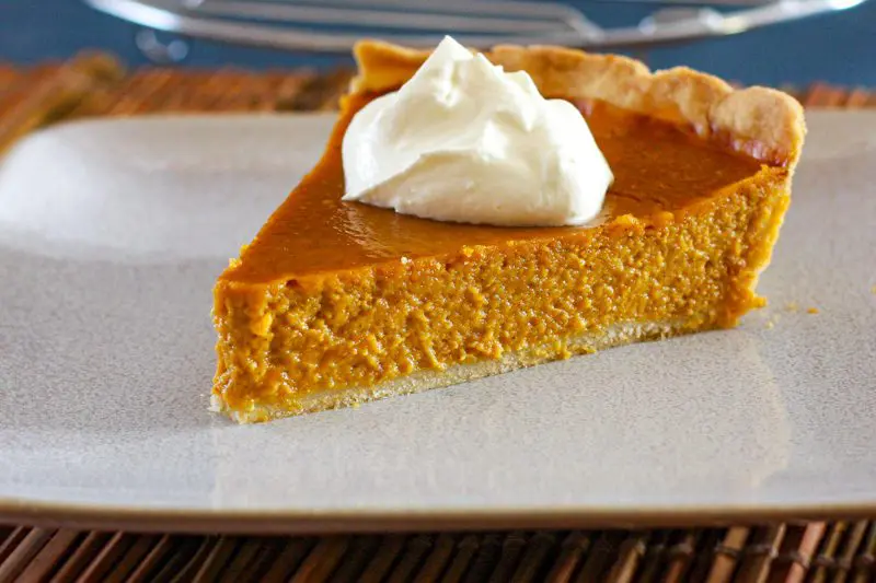 classic pumpkin pie with a dollopw of whipped cream.
