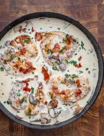 Cooked chicken breasts in a creamy wine sauce garnished with parsley and crispy prosciutto.