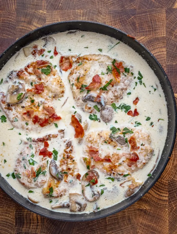 Cooked chicken breasts in a creamy wine sauce garnished with parsley and crispy prosciutto.