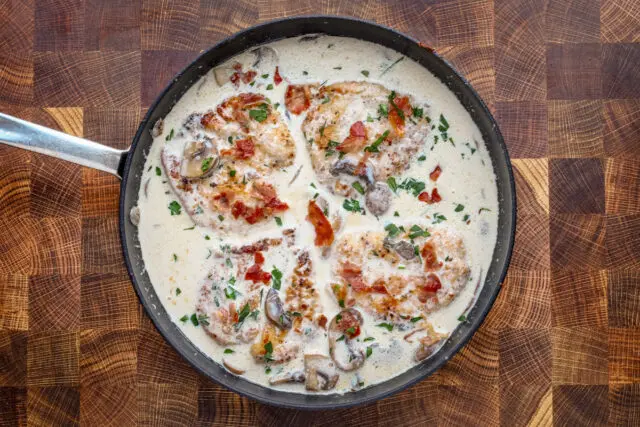 Cooked chicken breasts in a creamy wine sauce garnished with parsley and crispy prosciutto.