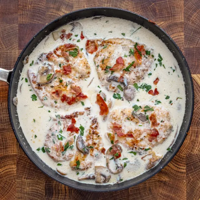 Cooked chicken breasts in a creamy wine sauce garnished with parsley and crispy prosciutto.