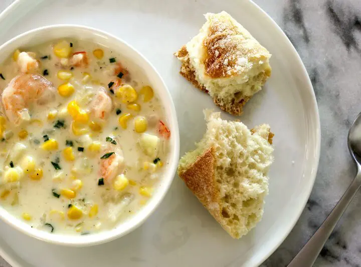 corn and shrimp chowder in a bowl with bread and chives for garnish