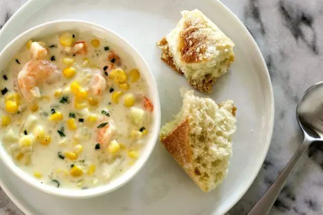 corn and shrimp chowder in a bowl with bread and chives for garnish