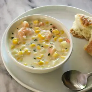 corn and shrimp chowder in a bowl with a torn baguette on the side.