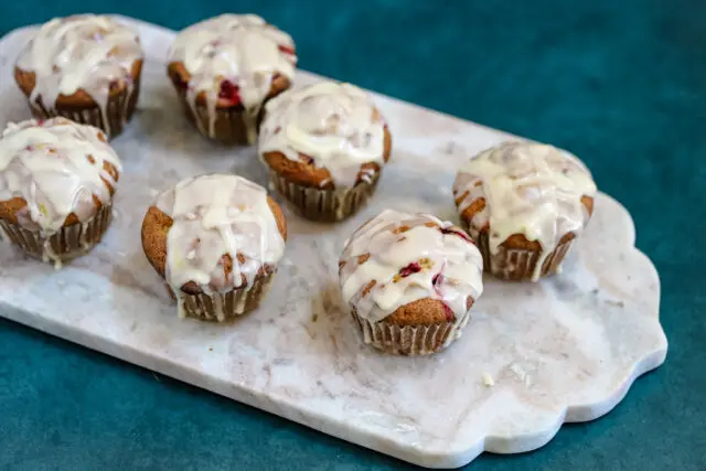 Glazed cranberry orange muffins shown on a marble slab .