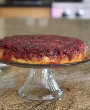 cranberry upside-down cake on a cake stand with plates for serving