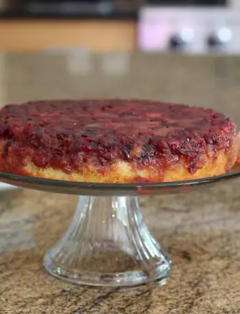 cranberry upside-down cake on a cake stand with plates for serving