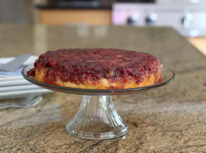 cranberry upside-down cake on a cake stand with plates for serving