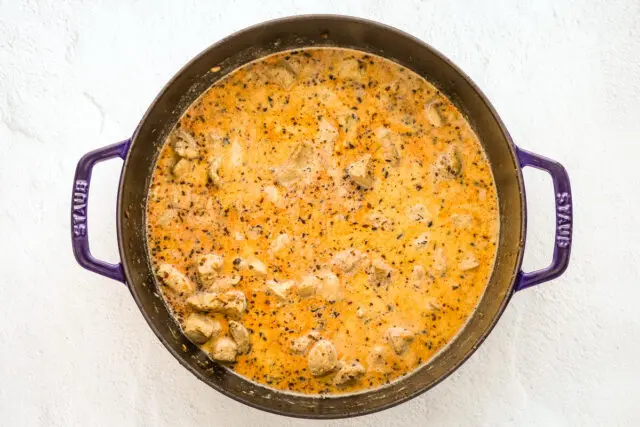 Adding the chicken, cream, seasonings, and broth to the sauté pan, making creamy Cajun chicken pasta with pancetta.