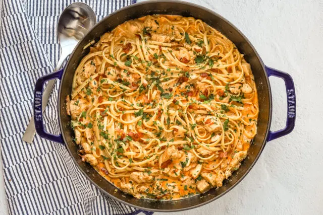 A sauté pan with creamy Cajun seasoned chicken and pasta with crispy pancetta, cream, garlic, and parsley.