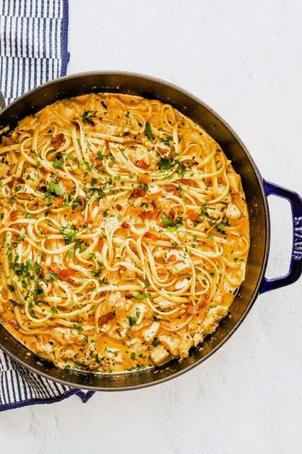 A sauté pan with creamy Cajun seasoned chicken and pasta with crispy pancetta, cream, garlic, and parsley.