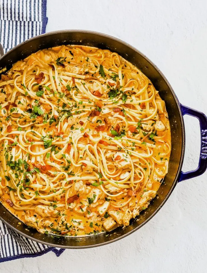 A sauté pan with creamy Cajun seasoned chicken and pasta with crispy pancetta, cream, garlic, and parsley.