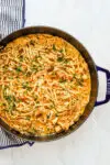 A sauté pan with creamy Cajun seasoned chicken and pasta with crispy pancetta, cream, garlic, and parsley.