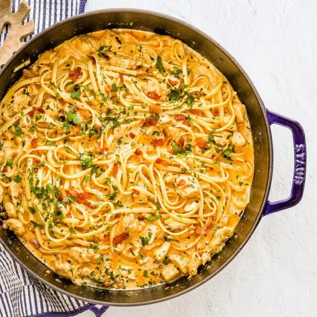 A sauté pan with creamy Cajun seasoned chicken and pasta with crispy pancetta, cream, garlic, and parsley.