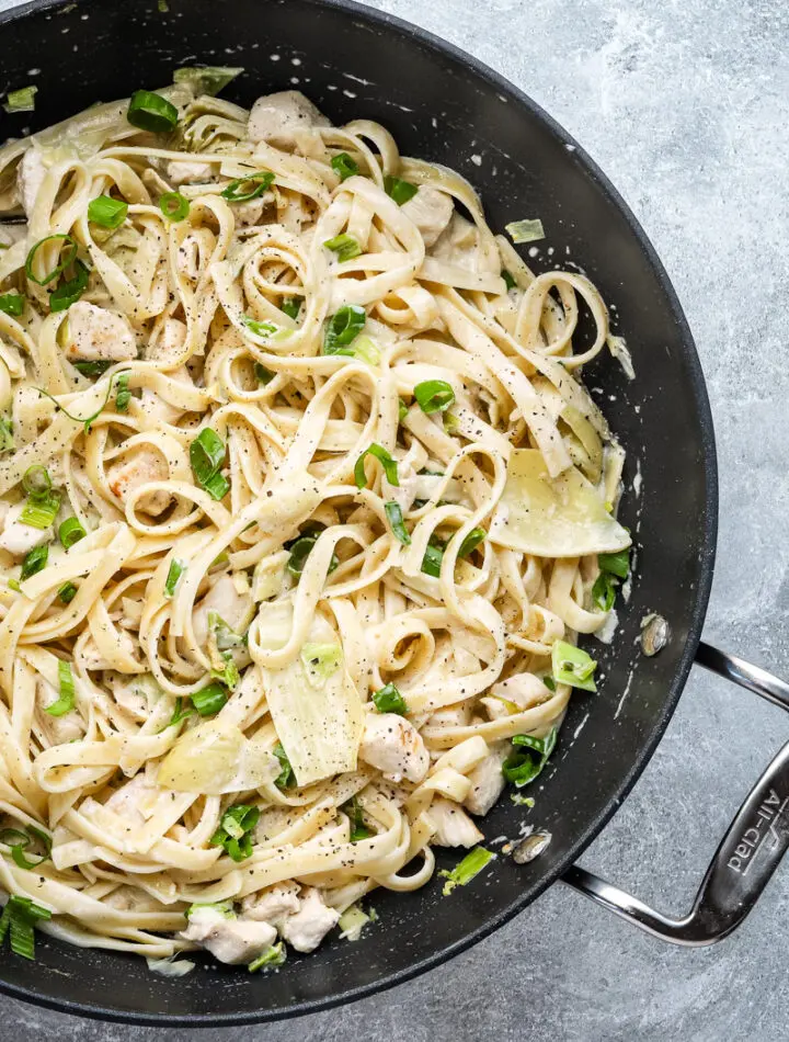 Closeup of creamy chicken pasta with artichokes and green onions.