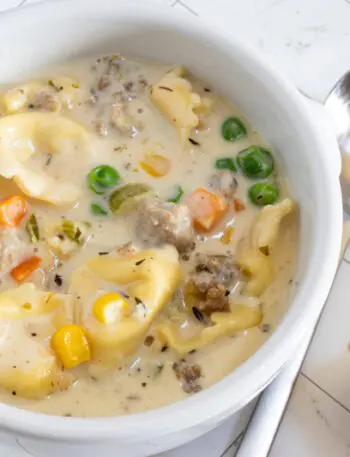 A bowl of sausage and tortellini soup with bread on the side.