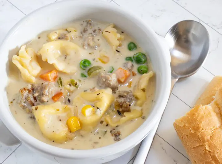 A bowl of sausage and tortellini soup with bread on the side.