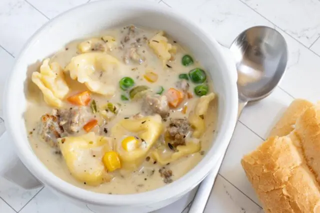 A bowl of sausage and tortellini soup with bread on the side.