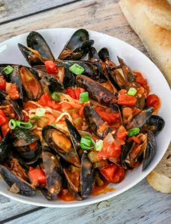 A bowl of mussels with Creole sauce, linguine, and a baguette on the side.