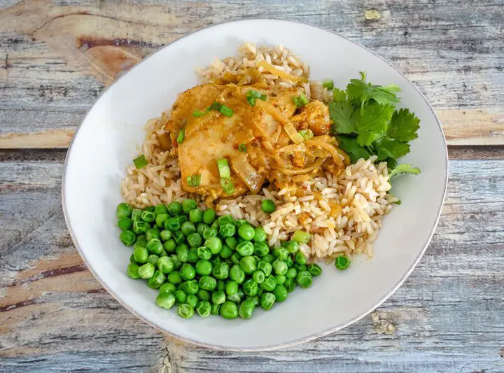 slow cooker chicken with curry flavor on a plate with rice and peas