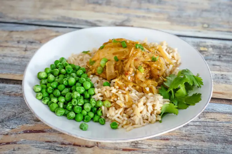 slow cooker curry chicken on a plate with peas and rice.