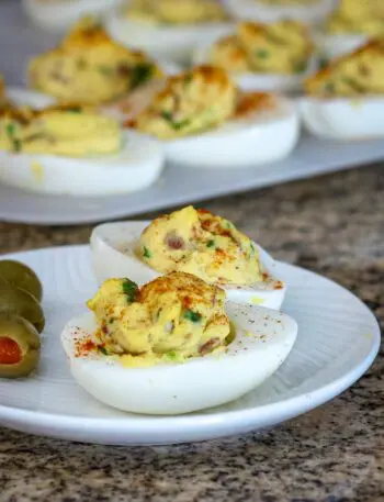 deviled eggs with bacon on a plate with more in the background