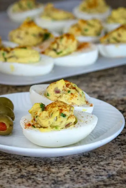 deviled eggs with bacon on a plate with more in the background