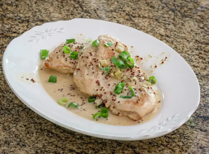 skillet dijon chicken with tarragon on a plate with green onion tops, garnishing it