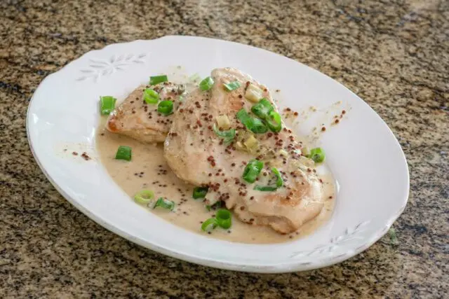 skillet dijon chicken with tarragon on a plate with green onion tops, garnishing it