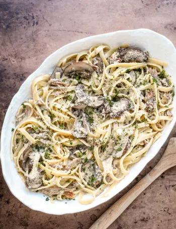 A serving dish of duck confit pasta made with duck confit legs, mushrooms garlic, shallots, fettuccine, garlic, cream, wine, and Parmesan cheese.